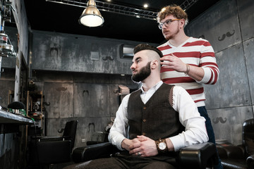 Hairdresser man shaves a client with a beard in a barbershop