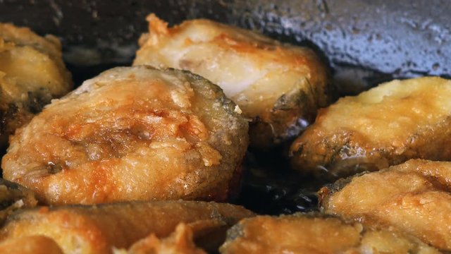 Frying hake fish outdoors on picnic, close up of frying pan with oil and fish slices