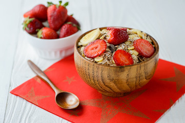 muesli with strawberry pieces in a wooden bowl, on a white wooden table