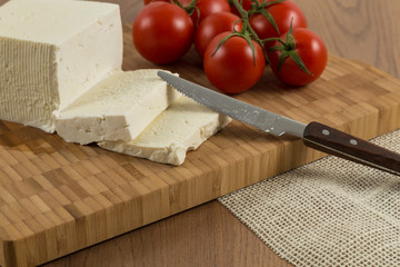 tomatoes and cheese slices and vegetables on wooden cutting board