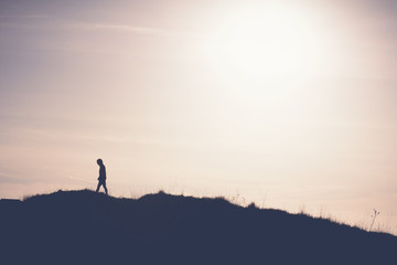 Man walking away from the sun on the hill. Artistic silhouette retro washout edit.