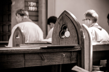 Gothic church pews with priests in the background out of focus. Artistic retro vintage edit.