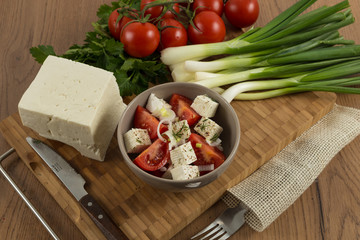 tomatoes and cheese salad with vegetables on wooden background