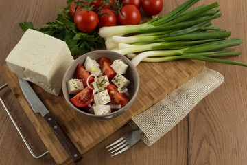 tomatoes and cheese salad with vegetables on wooden background