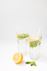 Homemade lemonade with water, lemon and mint leaves in two glasses on a white background.