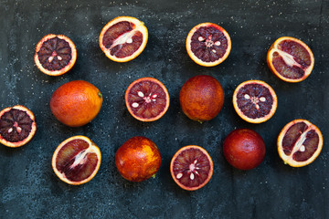 Red Sicilian orange whole and cut on a dark background with branches of rosemary. Daylight, open space for your text.