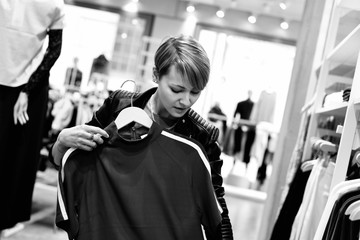 Junge, blonde Frau beim Shopping in einem Modehaus, betrachtet ein Oberteil