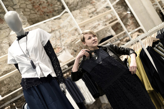 Junge, blonde Frau beim Shopping in einem Modehaus, betrachtet ein Kleid