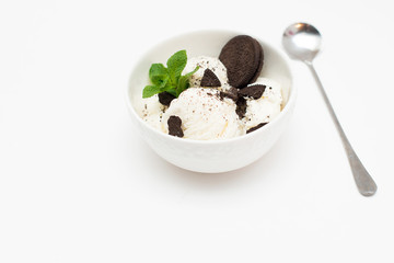 Homemade vanilla ice cream in a ceramic bowl with chocolate chip cookies and mint on a white background.