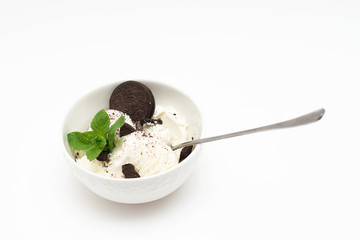 Homemade vanilla ice cream in a ceramic bowl with chocolate chip cookies and mint on a white background.