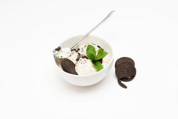 Homemade vanilla ice cream in a ceramic bowl with chocolate chip cookies and mint on a white background.