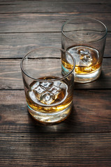 Two glasses of whiskey with ice cubes served on wooden planks. Vintage countertop and a glass of hard liquor