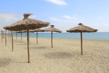 Fototapeta na wymiar Parasols à la plage/Parasols en paille à la plage avec sable fin et ciel bleu