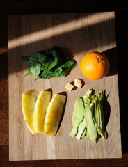 Orange, pineapple, avocado, spinach greens and fresh ginger on wooden board, top view