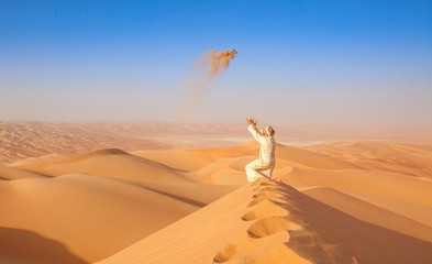 Fototapeta na wymiar arab man in local outfit throwing sand in the air in the arabian Desert