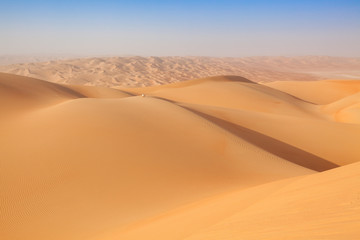 Arab man in traditional outfit sitting on a dune in the empty quarter of the arabian Desert