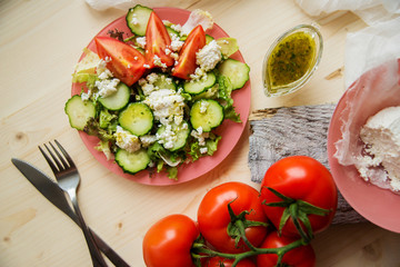 Greek salad in a glass salad bowl among ingredients for its cooking on an old wooden surface