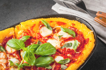 Italian Cuisine. Gluten-free food. Traditional national dish Pizza di polenta - pizza, cooked on corn polenta. On a black stone table, in a portioned skillet for baking. Top view copy space