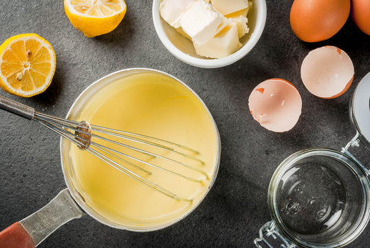 Traditional basic sauces. French cuisine. Hollandaise sauce in a metal saucepan, with ingredients for cooking - eggs, butter, lemons. On a black stone table. Copy space top view