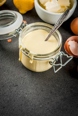 Traditional basic sauces. French cuisine. Hollandaise sauce in glass jar, with ingredients for cooking - eggs, butter, lemons. On black concrete stone table. Copy space