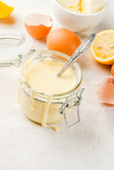Traditional basic sauces. French cuisine. Hollandaise sauce in glass jar, with ingredients for cooking - eggs, butter, lemons. On a white concrete stone table. Copy space