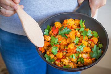 Woman holds a frying pan with vegetable ragout. Healthy food.