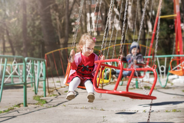 A little girl in a red dress is riding a carousel, a swing ride circuit.
