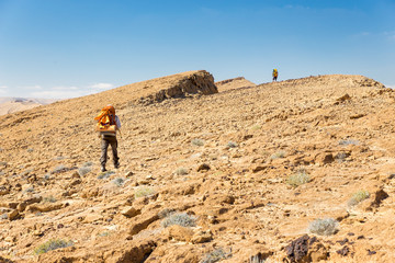 Fototapeta premium Two backpackers walking ascending mountain rock desert slope.