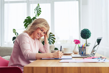 Pleased female with pretty smile writing in notebook while sitting at table