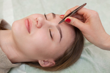 Obraz na płótnie Canvas Master makeup corrects, and gives shape to pull out with forceps previously painted with henna eyebrows in a beauty salon. Professional care for face