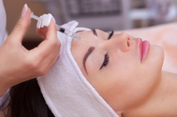 Obraz na płótnie Canvas The doctor cosmetologist makes the Botulinotoxin injection procedure for tightening and smoothing wrinkles on the face skin of a beautiful, young woman in a beauty salon.Cosmetology skin care.