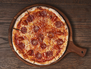 Hot pepperoni pizza on wooden board on table or wooden background. Flatlay or top view.