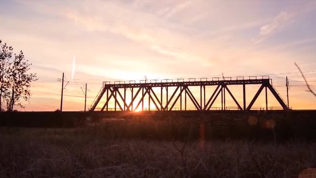 Panoramic view of train rides on rails through the bridge at sunrise. Timelapse. The train on the railway bridge.
