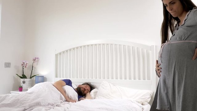Angry nervous pregnant woman waking up husband in bed