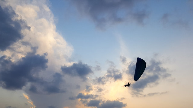 Silhouette of a male paraglider on a paraplan against a background of a sunset in the sky and clouds hovering over the sea. Concept: freedom, loneliness, hobby, sport.