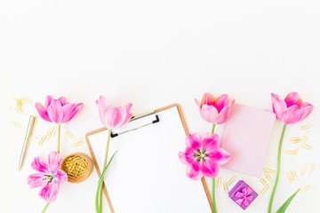 Beauty blog concept. Workspace with clipboard, notebook, pen, pink tulip flowers and accessories on white background. Flat lay, top view.