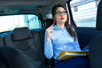 Beautiful young business woman in the car looking into contract papers..
