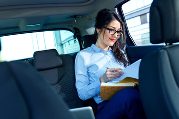 Fototapeta na wymiar Beautiful young business woman in the car looking into contract papers..