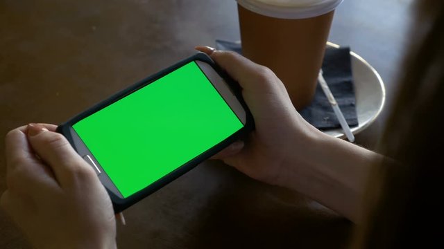 Woman watching a smart phone with chroma key green screen in landscape mode in a coffee shop