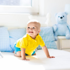 Baby boy playing on bed in sunny nursery