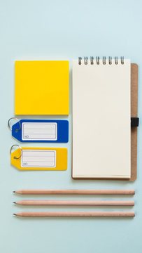 Notebook place on blue background with yellow post it, pencils and plastic tags