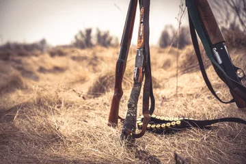 Poster Jachtscène met jachtgeweren en munitieriem op droog gras op het platteland tijdens het jachtseizoen als jachtachtergrond © splendens