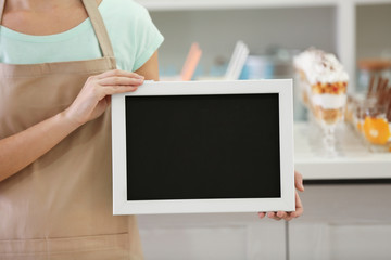 Female milk bar worker holding black chalk board on blurred background