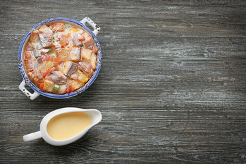 Freshly baked bread pudding in casserole dish and condensed milk on wooden table