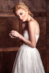 Naklejka premium Fashion beauty bridal shooting. Beautiful fashion bride in wedding dress posing in front of woody background standing near brown leather sofa. studio shot in vogue style. 