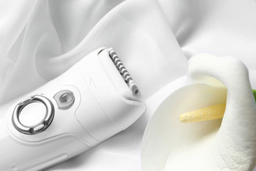Modern epilator and flower on cloth, closeup