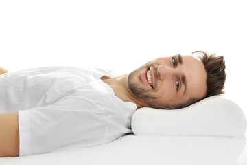 Fototapeta na wymiar Young man lying on bed with orthopedic pillow against white background. Healthy posture concept