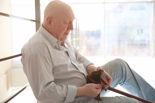 Senior man sitting near banisters with empty purse. Poverty concept