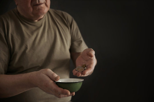 Senior man with bowl and coins on dark background, closeup. Poverty concept
