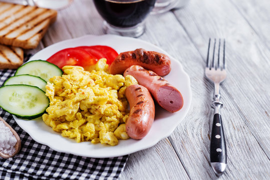 Hearty and traditional breakfast, scrambled eggs and milk with grilled pork, vegetables, tomato, cucumber, toast, juice and black coffee on a white wooden background
